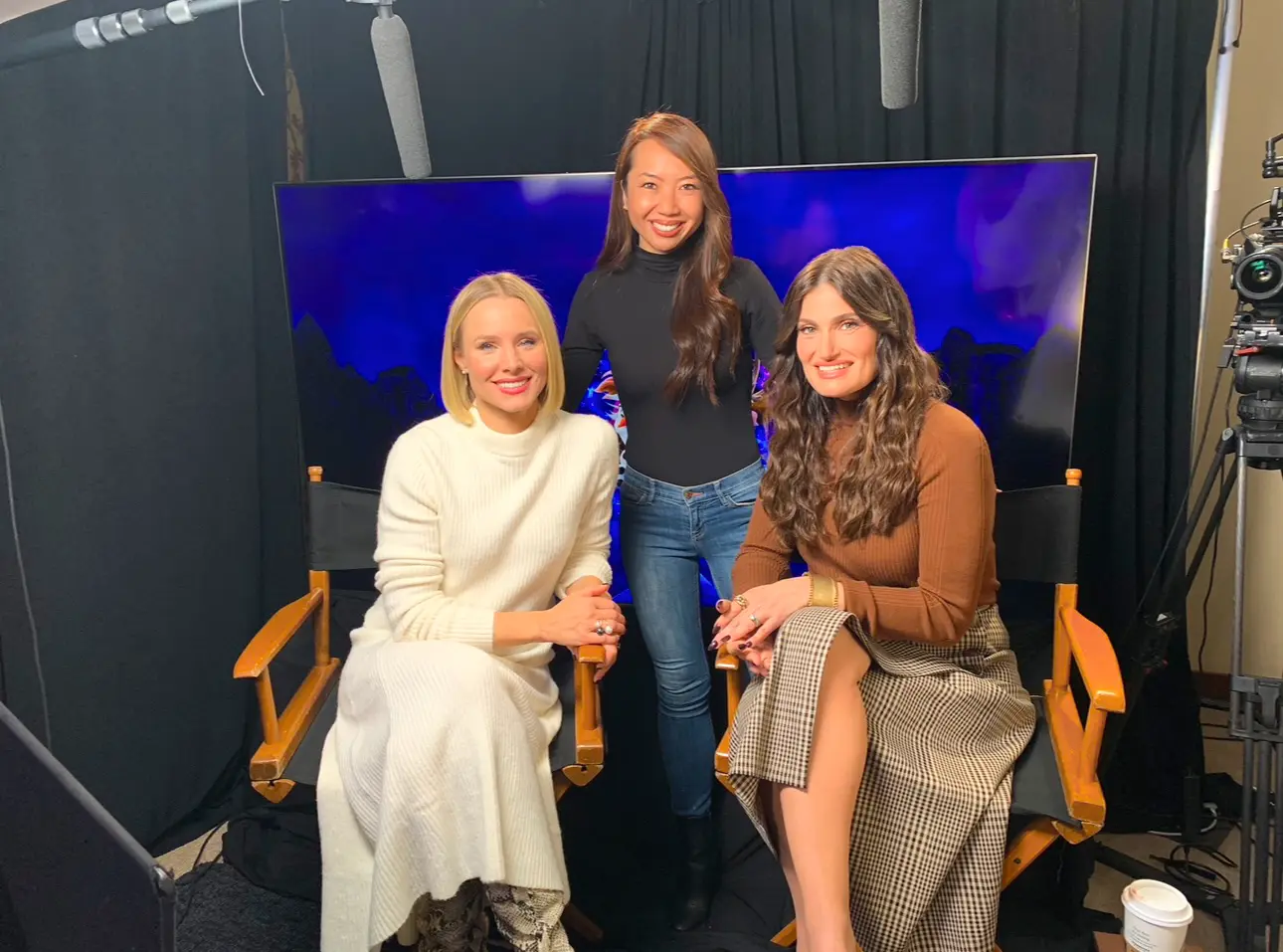 Three women sitting on a chair in front of a blue screen.