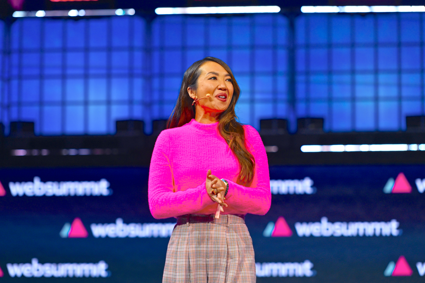 A woman in pink shirt and plaid skirt on stage.